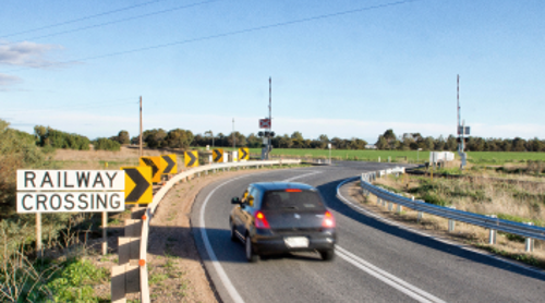 Car passing a bend in the road before level crossing